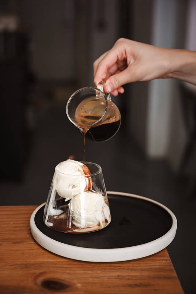a hand dripping chocolate from a small mug onto a cup of vanilla ice cream